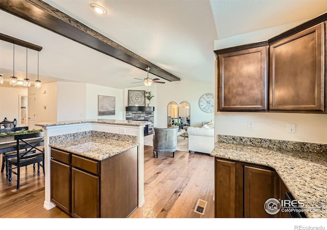 kitchen featuring beamed ceiling, ceiling fan, light stone countertops, and light wood-type flooring