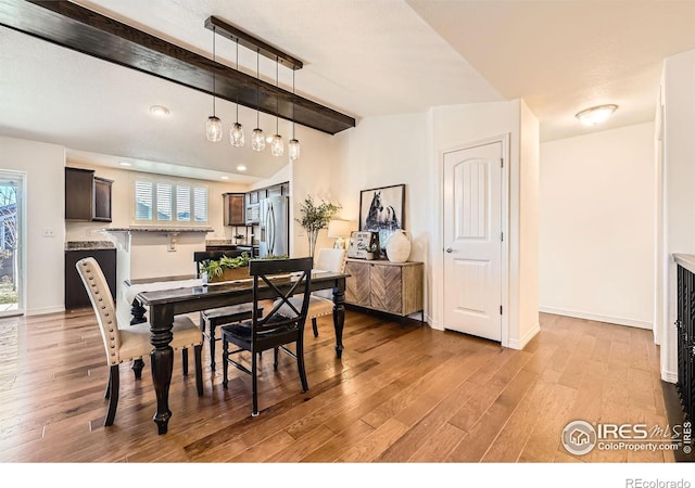 dining room with beamed ceiling, a textured ceiling, and light wood-type flooring