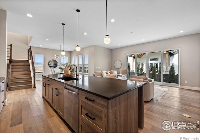 kitchen featuring dishwasher, decorative light fixtures, sink, a kitchen island with sink, and light wood-type flooring