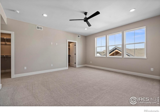 unfurnished bedroom with ceiling fan, light carpet, a closet, and a walk in closet