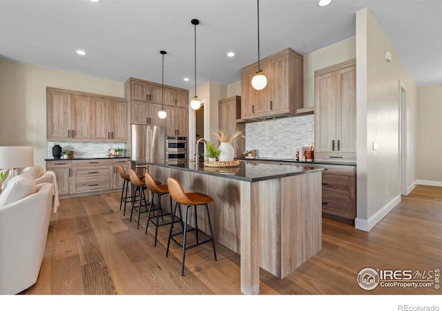 kitchen featuring stainless steel appliances, light hardwood / wood-style floors, tasteful backsplash, and a kitchen island with sink