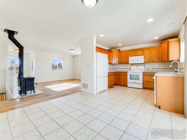 kitchen with a wood stove, sink, tasteful backsplash, light hardwood / wood-style flooring, and white appliances