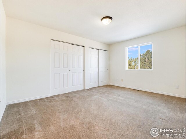 unfurnished bedroom with light colored carpet and two closets