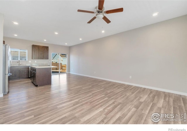 unfurnished living room with ceiling fan, sink, and light hardwood / wood-style floors