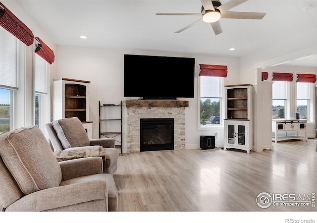 living room featuring a stone fireplace, a wealth of natural light, ceiling fan, and light hardwood / wood-style floors