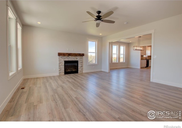 unfurnished living room with ceiling fan, a stone fireplace, and light wood-type flooring