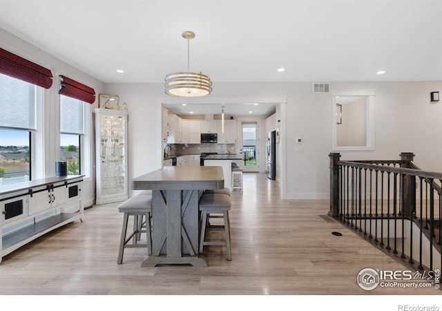 kitchen with white cabinetry, sink, stainless steel appliances, decorative light fixtures, and light wood-type flooring