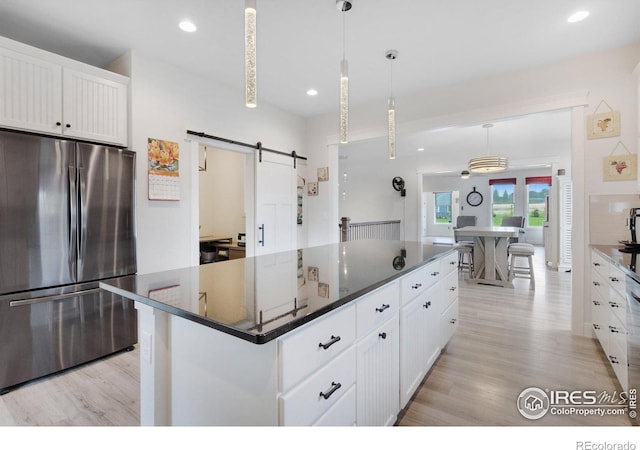 kitchen featuring a center island, hanging light fixtures, a barn door, white cabinetry, and stainless steel refrigerator