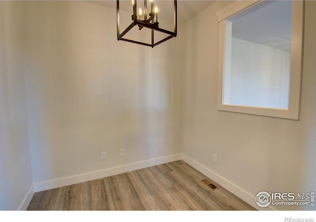 empty room with a notable chandelier and light hardwood / wood-style flooring