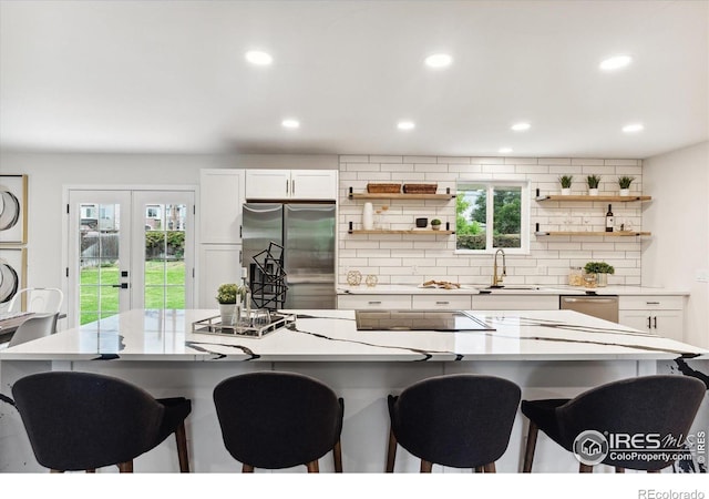 kitchen with black electric stovetop, a breakfast bar, stainless steel fridge, and white cabinetry