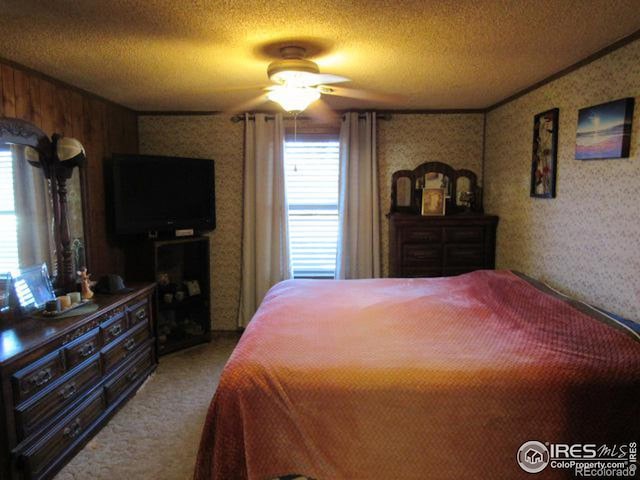 bedroom featuring a textured ceiling, multiple windows, wooden walls, and ceiling fan