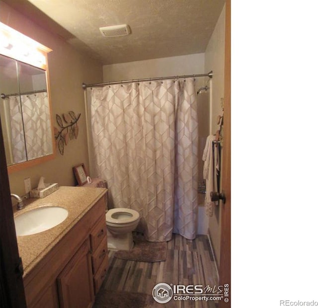 bathroom with walk in shower, a textured ceiling, toilet, vanity, and hardwood / wood-style flooring