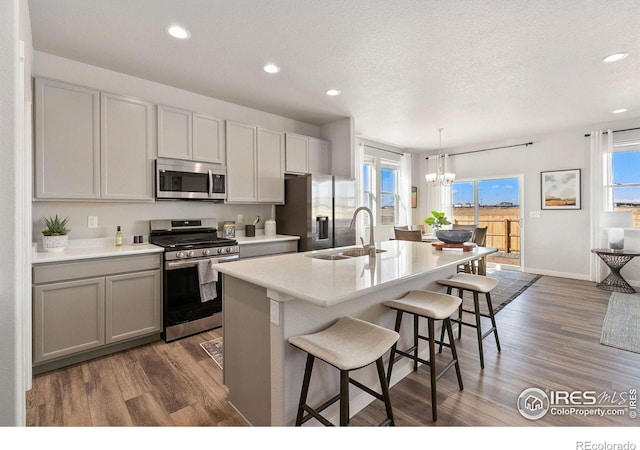 kitchen featuring appliances with stainless steel finishes, gray cabinetry, sink, a center island with sink, and decorative light fixtures