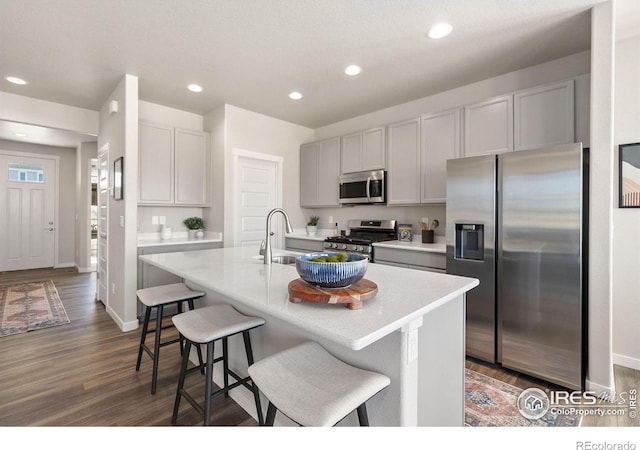 kitchen featuring a breakfast bar, a kitchen island with sink, appliances with stainless steel finishes, and dark wood-type flooring