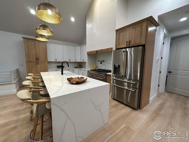 kitchen with decorative backsplash, sink, high end appliances, white cabinetry, and an island with sink