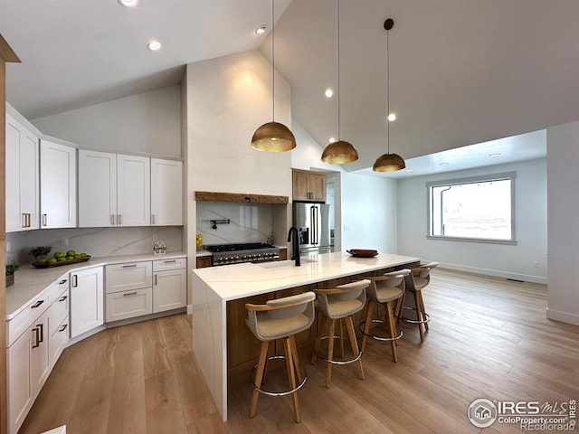 kitchen featuring tasteful backsplash, a center island with sink, sink, white cabinetry, and hanging light fixtures