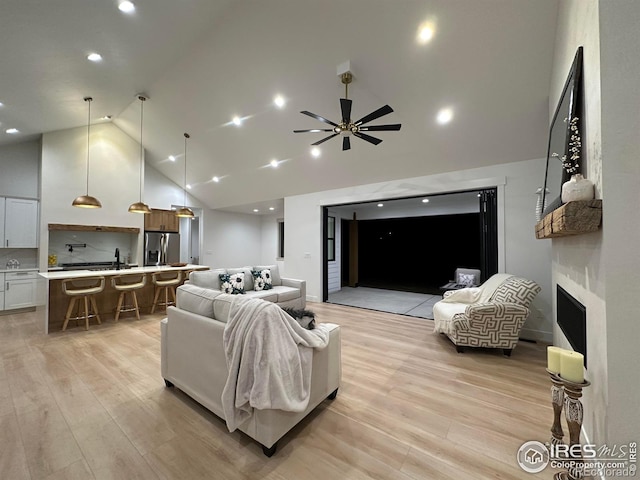 living room featuring ceiling fan, sink, light hardwood / wood-style flooring, and high vaulted ceiling