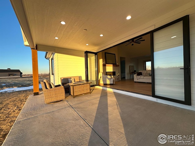 patio terrace at dusk with ceiling fan and an outdoor living space with a fireplace