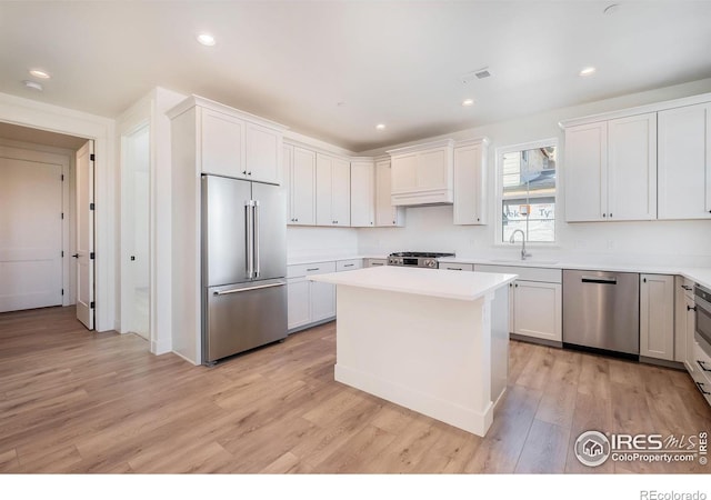 kitchen featuring sink, light hardwood / wood-style flooring, white cabinetry, stainless steel appliances, and a kitchen island