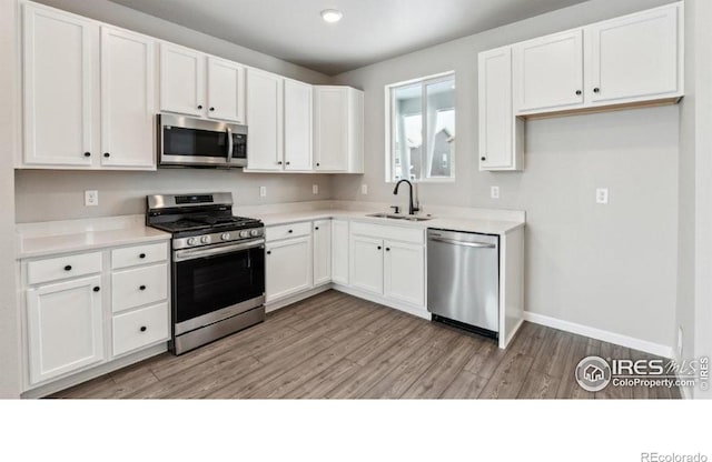 kitchen with stainless steel appliances, white cabinetry, sink, and light hardwood / wood-style floors