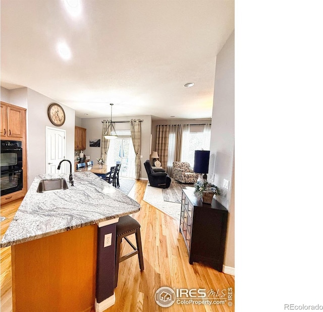 kitchen featuring a kitchen island with sink, sink, light hardwood / wood-style flooring, and black double oven