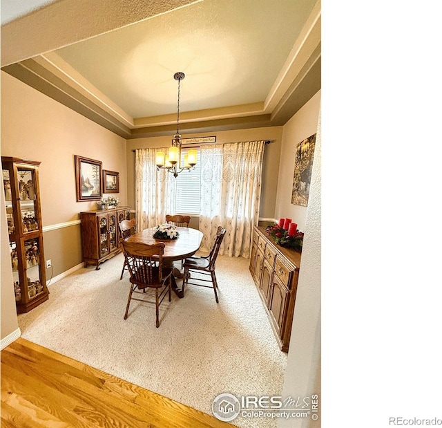 dining area featuring hardwood / wood-style flooring, a raised ceiling, and a chandelier