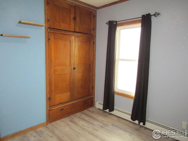 unfurnished bedroom featuring multiple windows, light hardwood / wood-style floors, and a baseboard heating unit