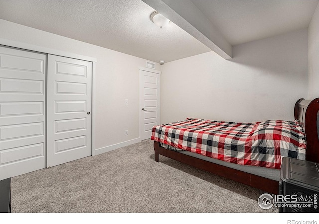 carpeted bedroom with beam ceiling, a textured ceiling, and a closet