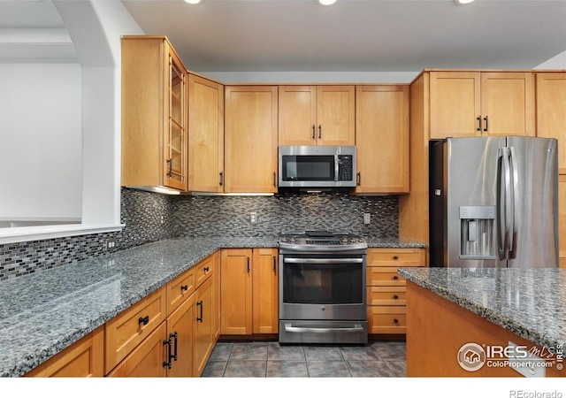 kitchen featuring light stone counters, appliances with stainless steel finishes, tasteful backsplash, and dark tile patterned floors