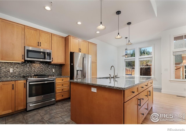 kitchen featuring decorative light fixtures, sink, backsplash, dark stone counters, and stainless steel appliances