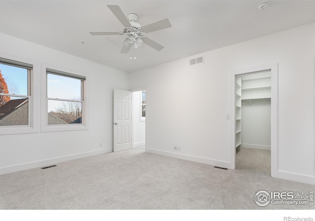 unfurnished bedroom featuring a walk in closet, light carpet, and ceiling fan