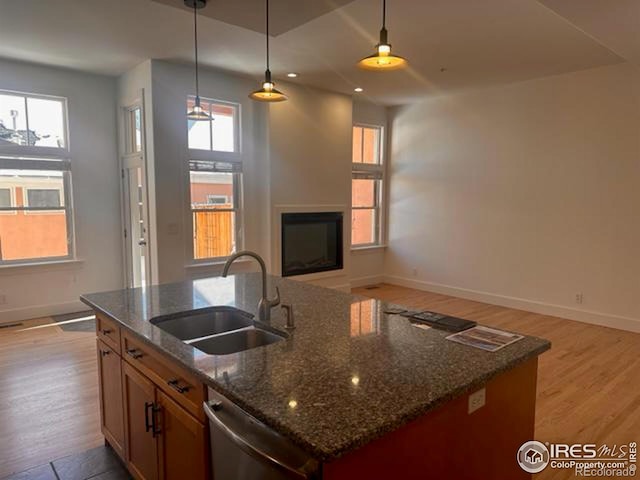 kitchen featuring pendant lighting, sink, a center island with sink, dark stone counters, and light wood-type flooring