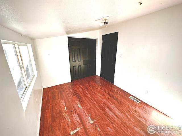 empty room featuring a textured ceiling, hardwood / wood-style flooring, and lofted ceiling