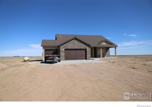 view of front of house featuring a garage, stone siding, roof with shingles, and dirt driveway