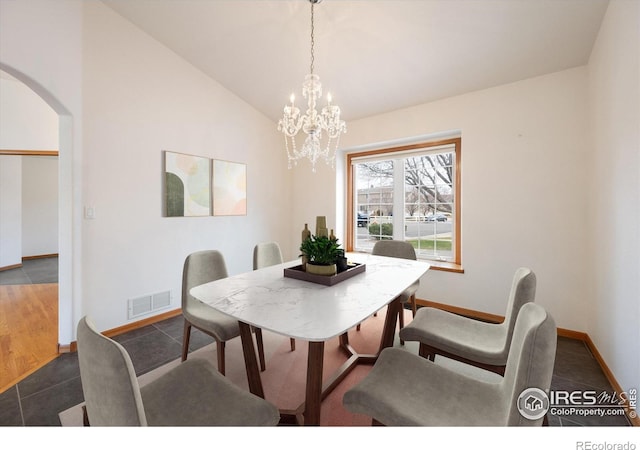 dining space with dark tile patterned flooring, an inviting chandelier, and vaulted ceiling