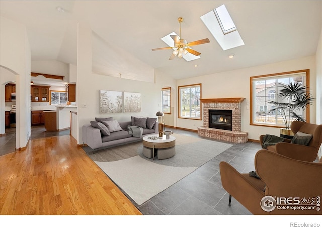 living room with hardwood / wood-style floors, ceiling fan, vaulted ceiling with skylight, and a fireplace