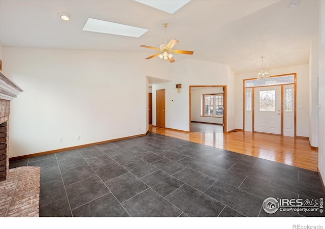 unfurnished living room featuring ceiling fan with notable chandelier, lofted ceiling with skylight, dark wood-type flooring, and a brick fireplace