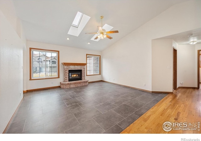 unfurnished living room with dark hardwood / wood-style flooring, a brick fireplace, ceiling fan, and vaulted ceiling with skylight