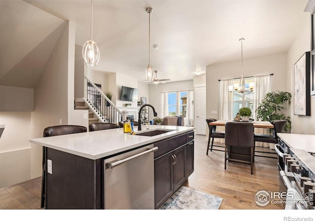 kitchen with a center island with sink, sink, hanging light fixtures, light hardwood / wood-style flooring, and stainless steel dishwasher