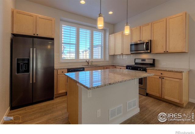 kitchen featuring appliances with stainless steel finishes, sink, pendant lighting, light hardwood / wood-style flooring, and a kitchen island