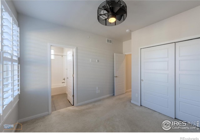 unfurnished bedroom featuring ensuite bathroom, light carpet, and a closet