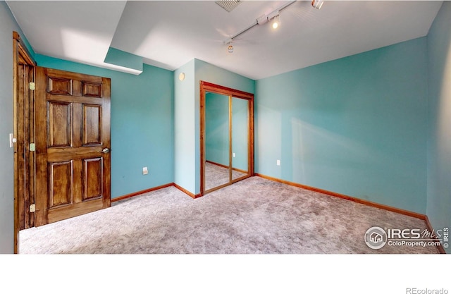 unfurnished bedroom with a closet, rail lighting, and light colored carpet