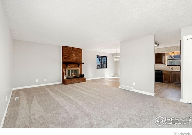 unfurnished living room featuring a fireplace, light colored carpet, a textured ceiling, and a notable chandelier