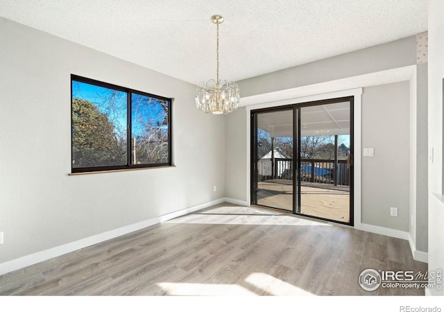 spare room with light hardwood / wood-style flooring, a textured ceiling, and an inviting chandelier