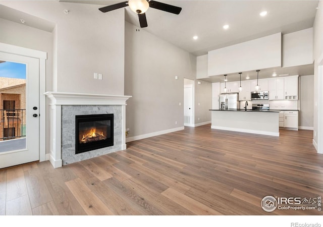 unfurnished living room featuring a towering ceiling, ceiling fan, sink, light hardwood / wood-style flooring, and a premium fireplace