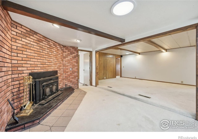 unfurnished living room with beamed ceiling, light colored carpet, a wood stove, and brick wall