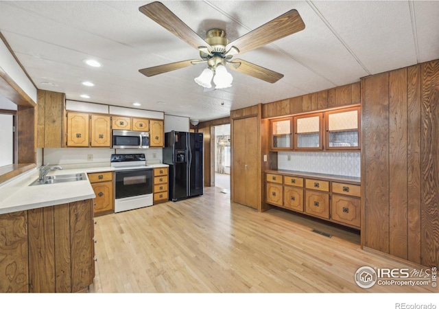 kitchen with black fridge with ice dispenser, wooden walls, sink, electric range, and light hardwood / wood-style floors