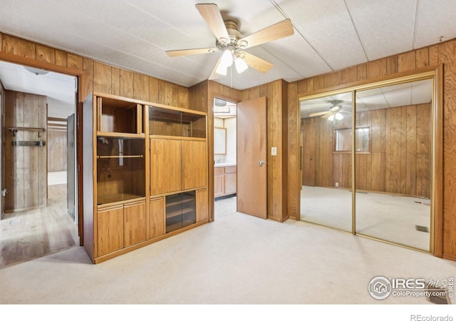 unfurnished bedroom featuring wooden walls, a closet, carpet floors, and ceiling fan