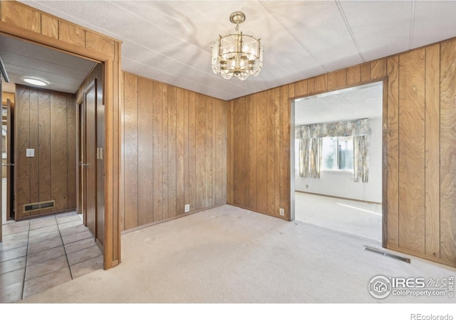 carpeted empty room with wood walls and an inviting chandelier