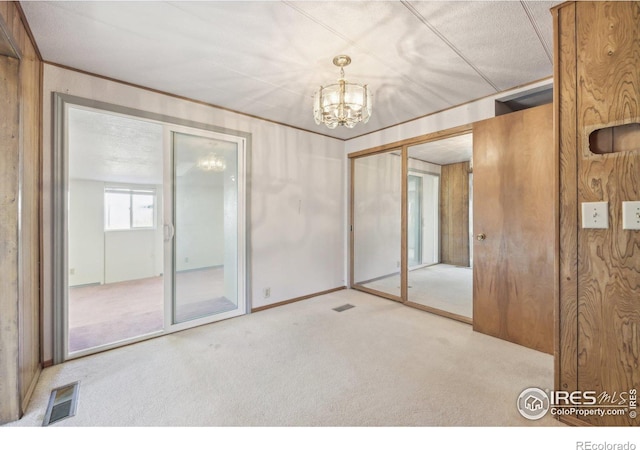 carpeted spare room featuring wooden walls and a notable chandelier